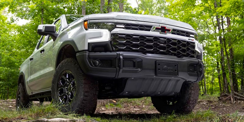 White Chevrolet Silverado driving in woods.